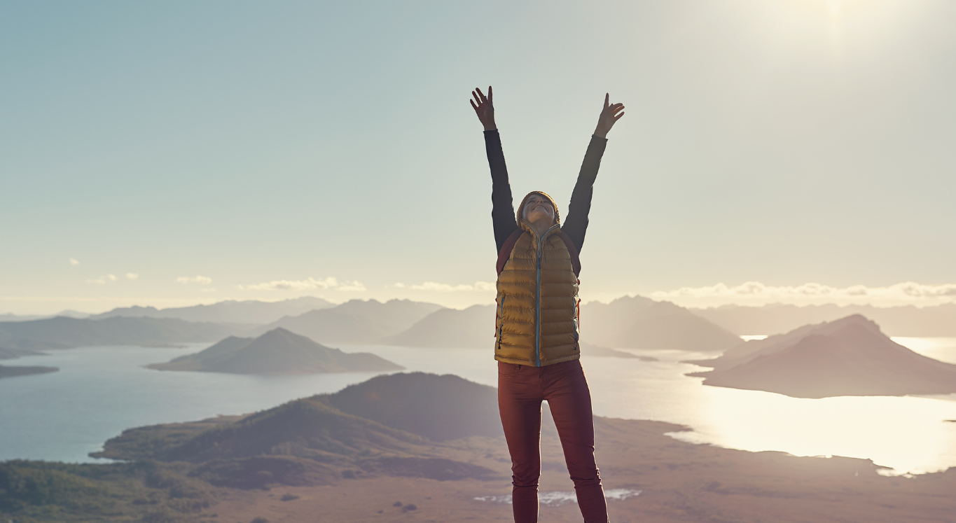 Lady extending her arms up standing on mountain top